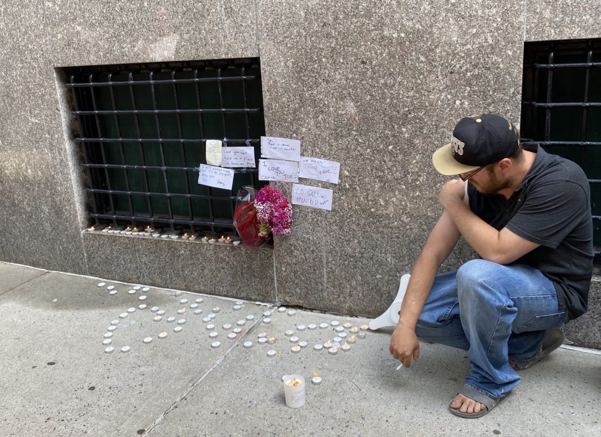 John Grima kneels near a memorial for a homeless friend who dies